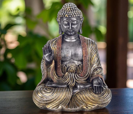 Figura de Buda plateado en posición de meditación con mano alzada, símbolo de bendición y calma interior